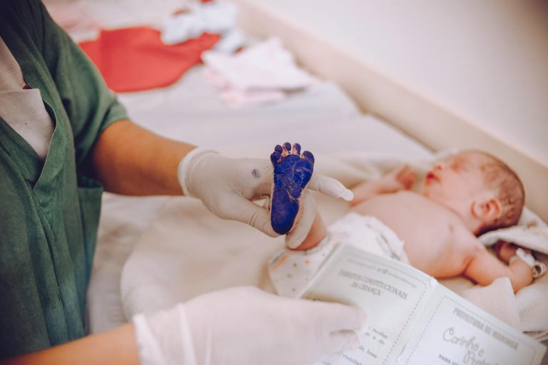 Medical professional taking footprint of a newborn baby in hospital setting.